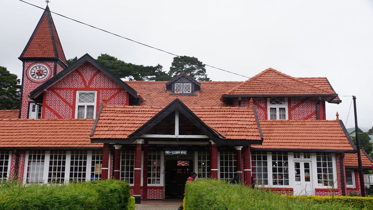 Red-roofed building with a clock tower and decorative elements, surrounded by greenery.